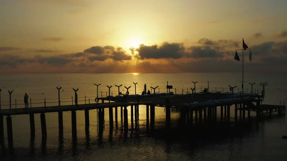 Drone Shows Pier with People Making Selfies Against the Sunrise Silhouette