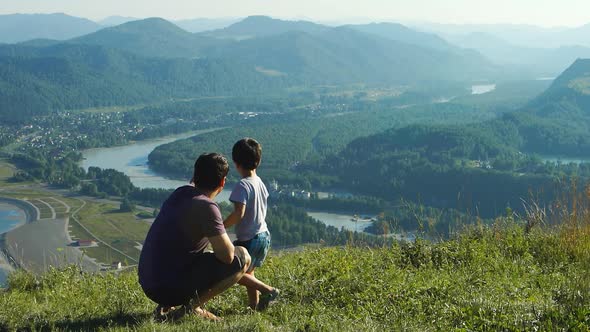 Father With Son Are Looking To The Mountains And River