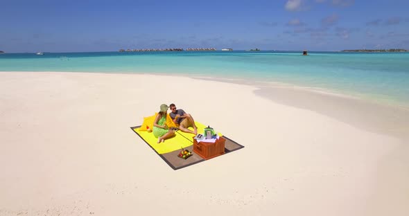 Aerial drone view of a man and woman couple having a picnic meal on a tropical island beach