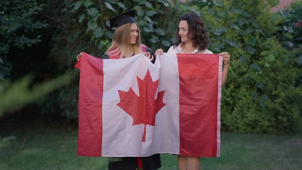 Portrait of Happy Smiling Mature Mother and Young Graduate Daughter Posing with Canadian Flag on