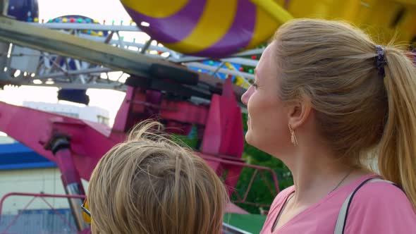 Closeup of a Mother and Son in an Amusement Park Standing By a Carousel That Spins Very Quickly