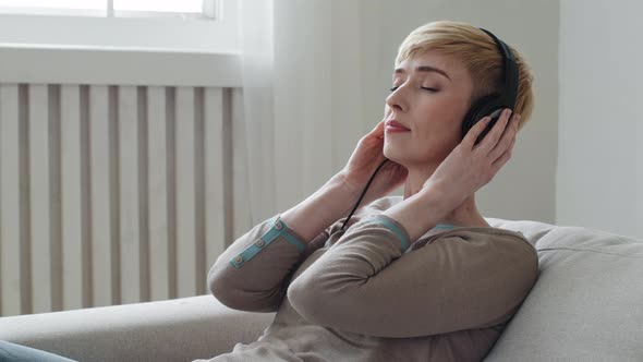 Calm Serene Young Adult Woman Relaxing on Comfortable Sofa Eyes Closed Wear Headphones Enjoy Listen