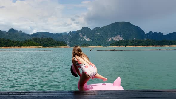 Funny Young Woman in Swimwear Sitting on Pink Inflatable Flamingo at Blue Lake