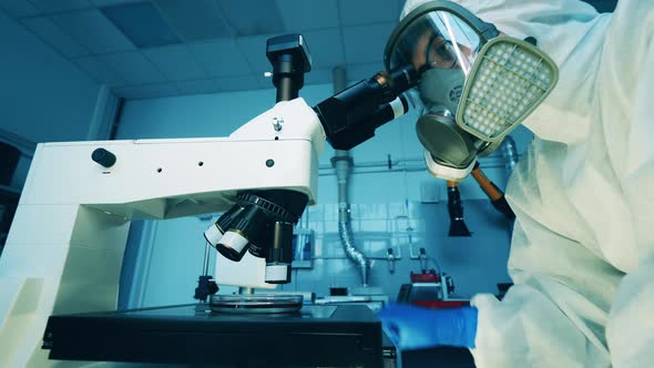 A Man in a Hazmat Suit is Operating a Microscope in a Laboratory