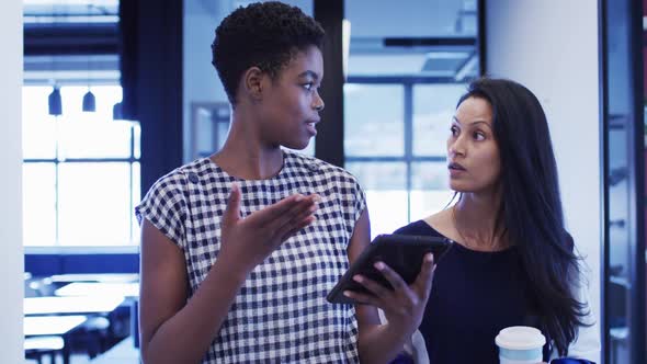 Diverse businesswomen talking using digital tablet walking through office