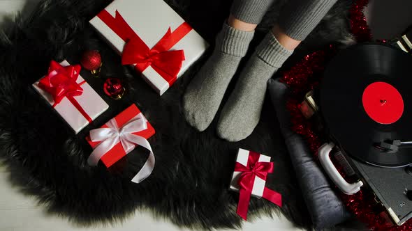 Woman in Warm Cozy Socks Sits on a Gray Fur Skin Near a Retro Turntable. Presents, Jewelry and