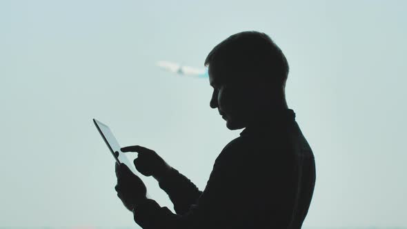 Silhouette of Young Men Using Tablet Pc on the Background of an Airplane Taking Off.