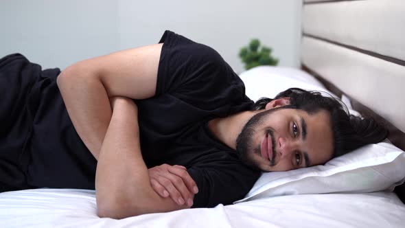 Indian man smiles at the camera while lying down on the bed