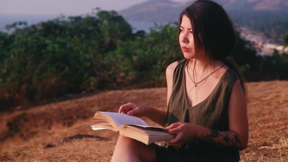 One asian woman sits on the hill and reading a book with sea view