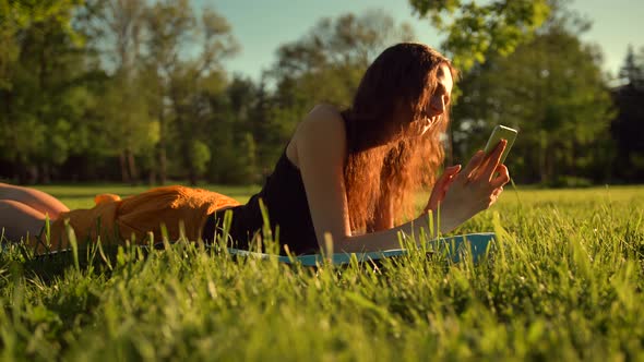 Happy Girl Typing Sms Lying in Park on Grass. Woman Chatting in Telephone.