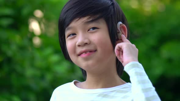 Asian Child With Hearing Aid Behind The Ear Outdoors