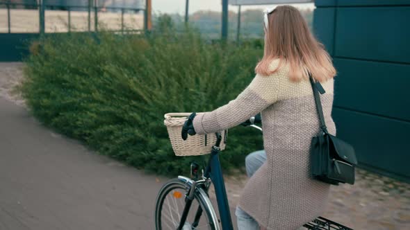 Woman Is Riding By Bicycle in City in Empty Modern Street in Autumn Morning