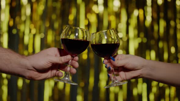Two Hands with Glasses of Red Wine Making Cheers Raising Toast on Gold Background in Slow Motion