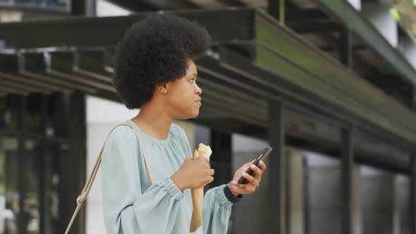 African american businesswoman eating and using smartphone