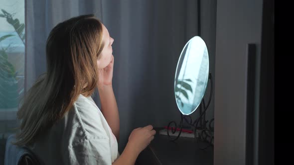 Young Woman Looks at Herself in the Mirror Examines the Skin of Her Face and Gets Upset