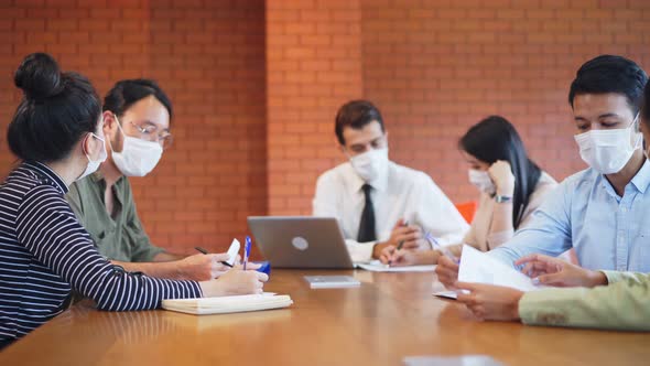 Group of Asian young business people wear face mask and working on computer in office workplace.