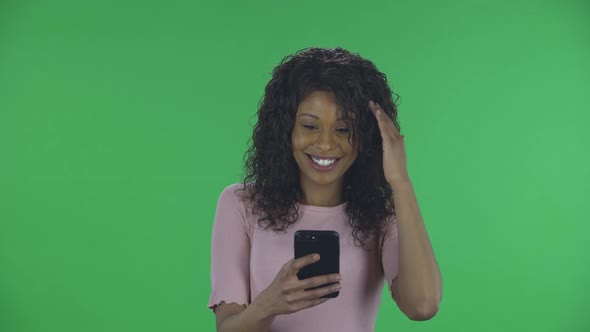 Portrait of Beautiful African American Young Smiling Woman Is Texting on Her Phone and Rejoice