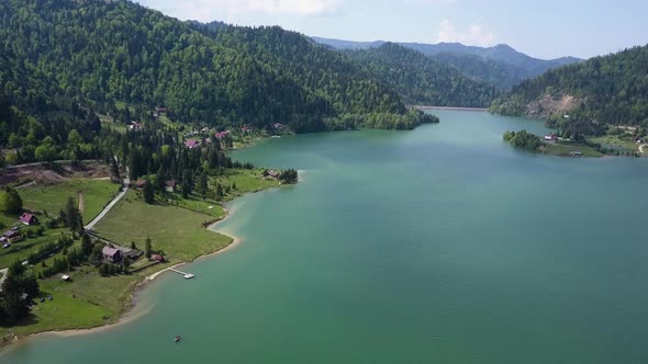 Aerial Slow Panning shot of Lake with clear water and trees in the background in the valley