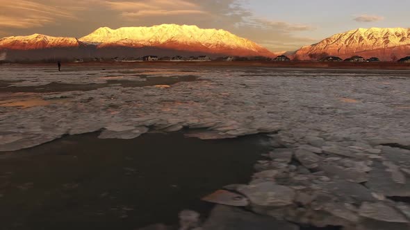 Panning view of ice chunks on shore of lake reflecting snow capped mountain