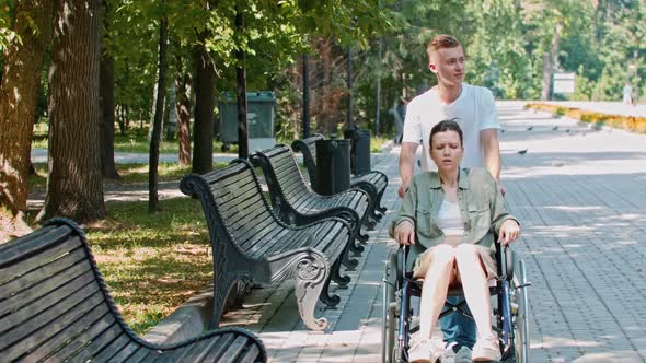 A Couple Walking in Park  a Guy Rides a Woman in a Wheelchair