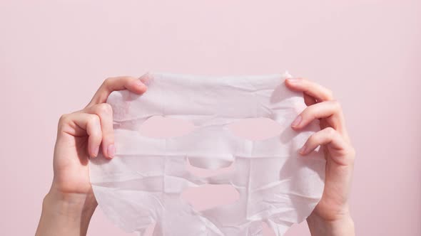 Female hands holding sheet of white mask on pink background. Stop motion animation.