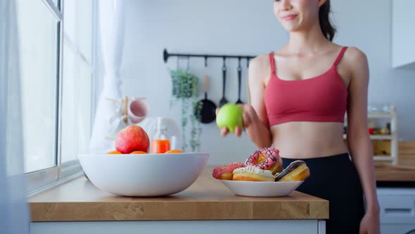 Beautiful sport girl in sportswear desire to chose fruit and ignore sweet donut, enjoy healthy foods