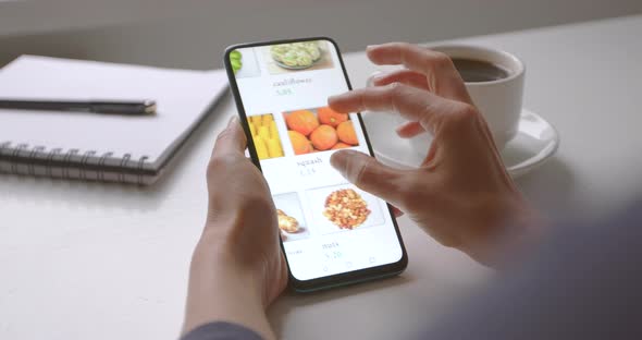 Online shopping. A woman from home buys food in an online store choosing on a smartphone