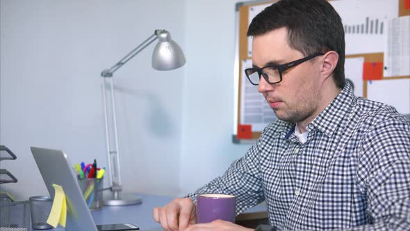 The Manager Typing Text on the Laptop Sitting at His Working Place.