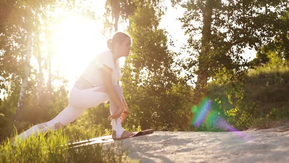 Attractive Young Woman Is Doing Yoga Asana Pose of Warrior Background of Bright Sunray and Trees