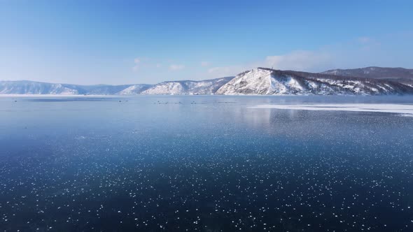 Flying over lake ice. The blue sky is reflected in it. Duck swim in the ice hole