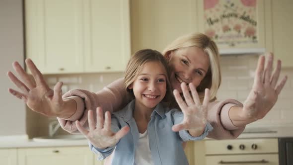 Happy Mother and Little Daughter Showing Hands in White Flour at Camera Cooking Dough Smiling