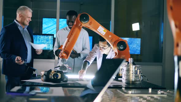 Group of Male Scientists Are Watching a Robotic Arm While Drawing