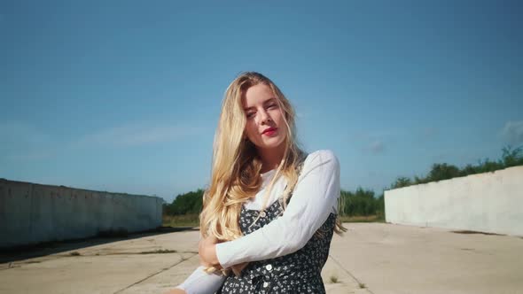 A Young Girl in a Beautiful Dress is Standing Near Concrete Walls and a Field