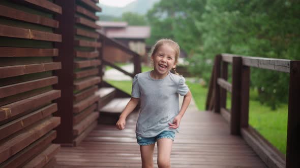 Joyful Little Girl Runs to Camera Along Veranda Floor