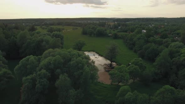 View of Forest, Lake and Country Houses Against Blue Sky with Sun and Clouds in Sunset at Summer