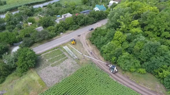 High Angle View of a Dirt Road with an Excavator Dragging a Pole Construction