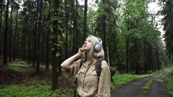 Blond hair woman in headphones with backpack in rainy forest