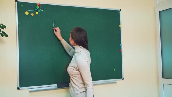 Smiling teacher stands near the blackboard in the classroom.