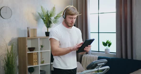 Sporty Bearded Man in Headset Browsing Information on Tablet PC while Training on Treadmill