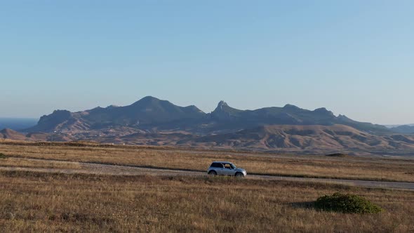 A Small Car Rides on the Road Against the Backdrop of the Mountains