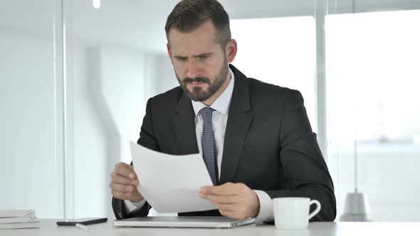 Pensive Middle Aged Businessman Reading Documents in Office Paperwork
