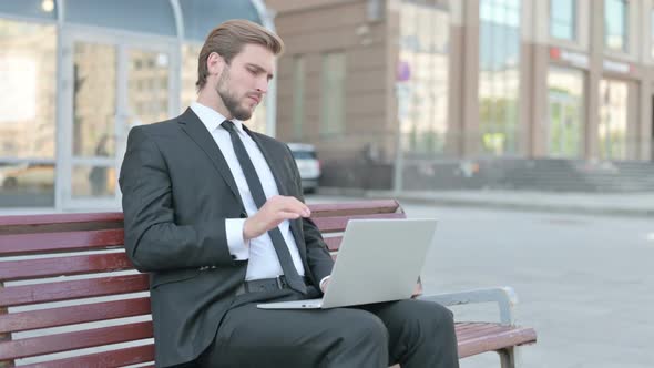 Businessman with Neck Pain Using Laptop While Sitting Outdoor on Bench
