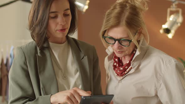 Young and Senior Female Coworkers Using Tablet and Talking
