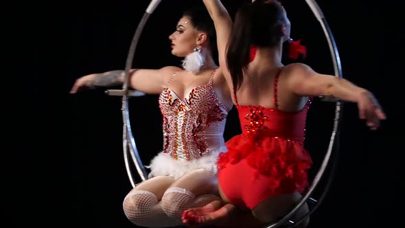 Two Flexible Gymnasts Trick on the Aerial Hoop Metal Construction. Black Background. Slow Motion