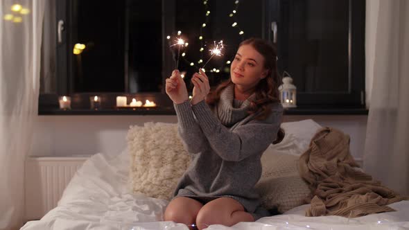 Happy Young Woman with Sparklers in Bed at Home