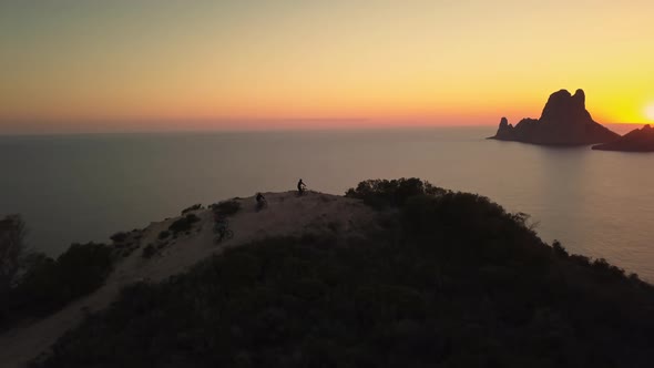 Mountain bikers reach epic trail peak, celebrate, golden Es Vedra drone