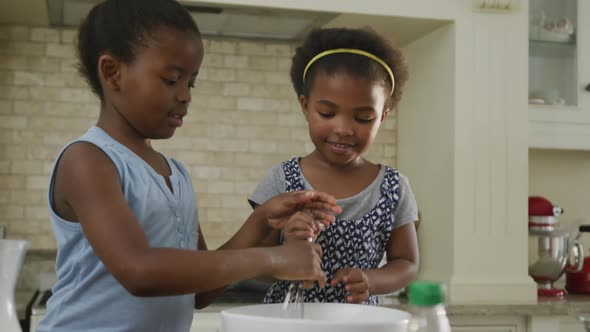 Happy two african american girls baking and mixing ingredients in kitchen