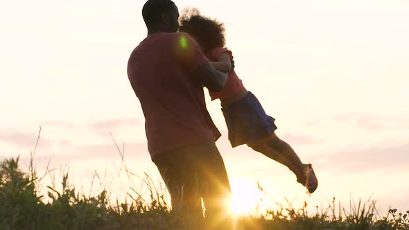 African-American Dad Playing With His Little Daughter in Bright Rays of Sunset