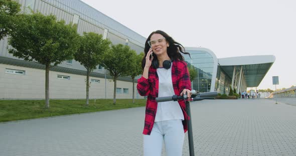 Woman in Casual Clothes which Walking with Her Personal E-scooter and Talking on Phone