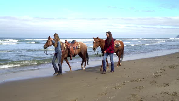 Women walking with horses at beach